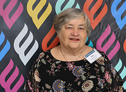 A photo of Judy Messing posed in front of a colorful backdrop.