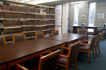 Image: Long table surrounded by chairs. Bookcases in background.